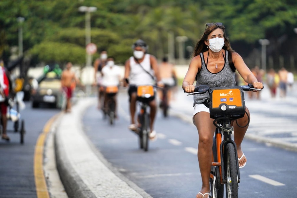 Mulher pedalando uma bicicleta preta com laranja na orla do Rio de Janeiro para exemplificar a ciclomobilidade.